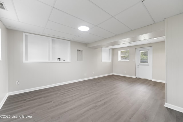 interior space with baseboards, a drop ceiling, and dark wood-type flooring
