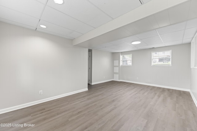 below grade area with baseboards, a drop ceiling, and wood finished floors