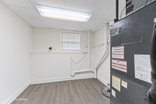 interior space with baseboards, heating unit, a drop ceiling, and wood finished floors