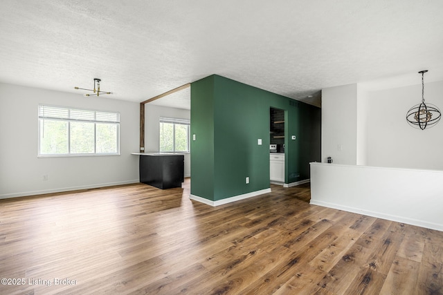 unfurnished living room with a chandelier, wood finished floors, a textured ceiling, and baseboards