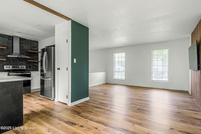 unfurnished living room featuring a textured ceiling, light wood finished floors, and baseboards