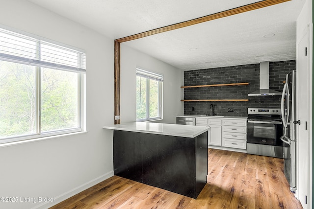 kitchen with appliances with stainless steel finishes, open shelves, white cabinetry, wall chimney exhaust hood, and a sink