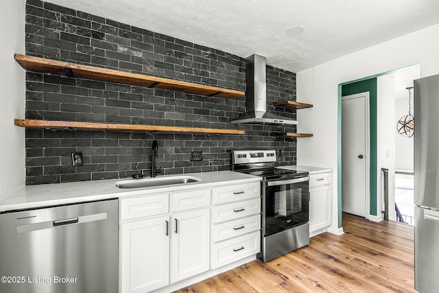 kitchen featuring appliances with stainless steel finishes, open shelves, wall chimney exhaust hood, a sink, and light wood-style floors