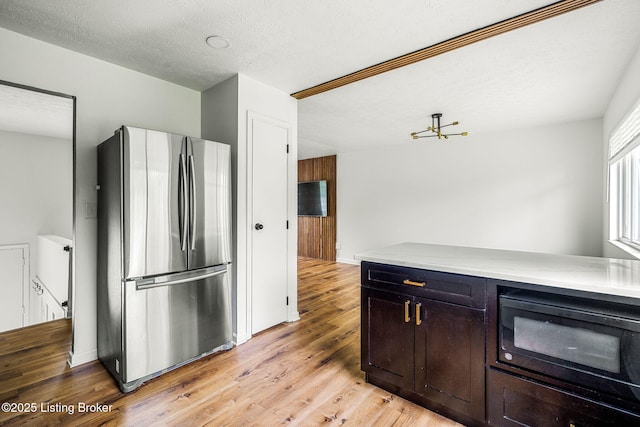 kitchen with freestanding refrigerator, black microwave, light wood finished floors, and a textured ceiling
