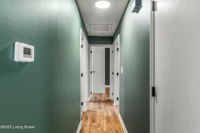 hall featuring attic access, light wood-type flooring, and baseboards