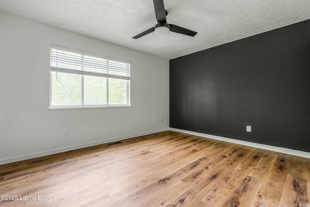 empty room with light wood-style flooring, a textured ceiling, baseboards, and ceiling fan
