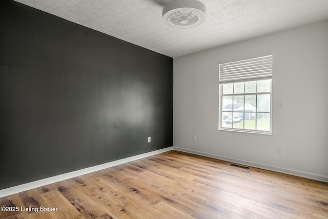 spare room with a textured ceiling, light wood finished floors, and baseboards