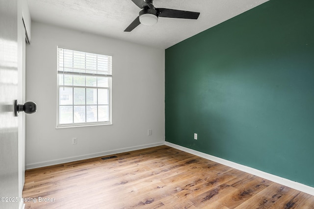 empty room with a ceiling fan, wood finished floors, a textured ceiling, and baseboards