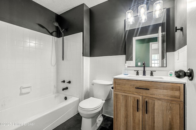 bathroom with tile walls, toilet, vanity, shower / bathtub combination, and a wainscoted wall