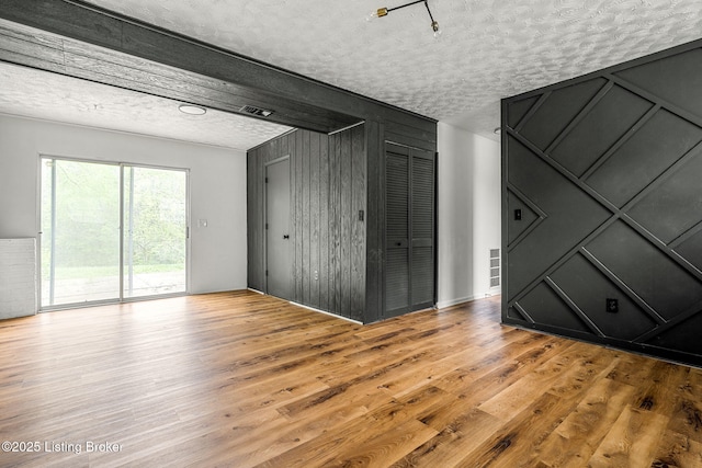 unfurnished living room with a textured ceiling, wood finished floors, and wood walls