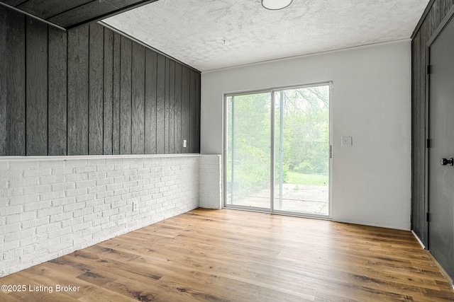 unfurnished room with wood finished floors, wood walls, and a textured ceiling