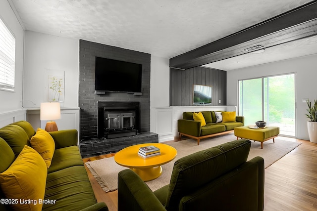 living room featuring wood finished floors, healthy amount of natural light, beam ceiling, and a fireplace