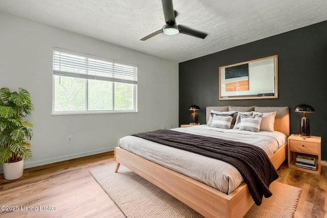 bedroom featuring baseboards, wood finished floors, a textured ceiling, and ceiling fan