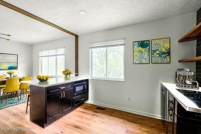 kitchen featuring open shelves, a textured ceiling, black microwave, a peninsula, and light wood finished floors