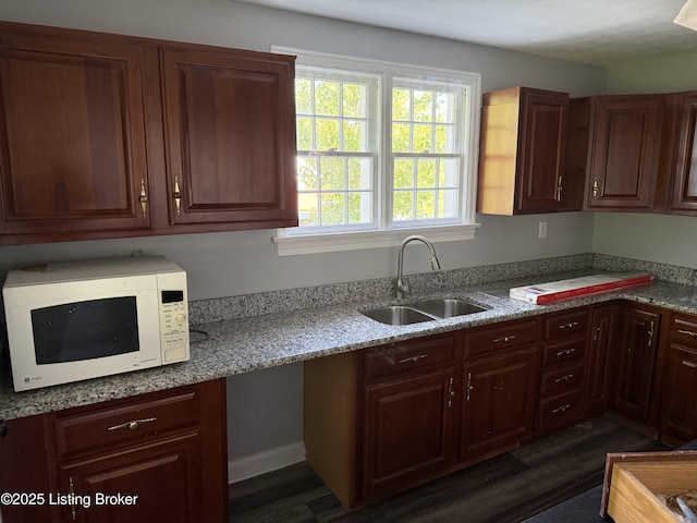 kitchen with a sink, light stone counters, white microwave, and dark wood-style floors