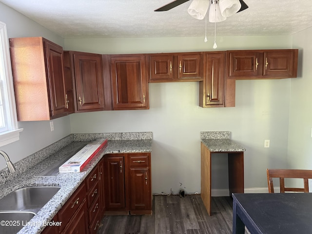 kitchen with ceiling fan, a textured ceiling, a sink, light stone counters, and dark wood-style floors