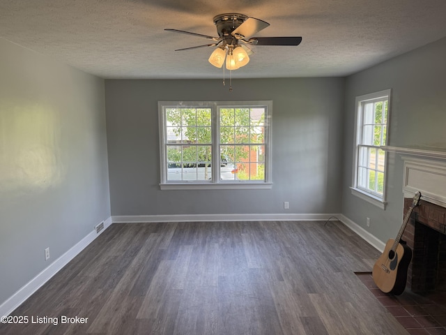 unfurnished living room with visible vents, a fireplace, ceiling fan, dark wood-style floors, and a textured ceiling