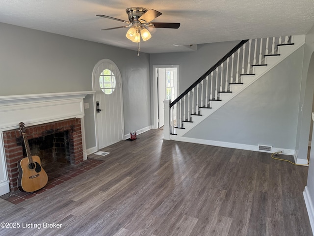 unfurnished living room with a ceiling fan, wood finished floors, a fireplace, and stairway