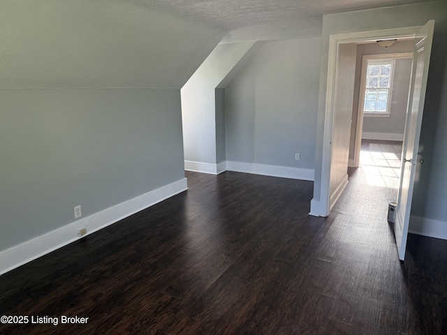 bonus room featuring baseboards, dark wood finished floors, a textured ceiling, and lofted ceiling