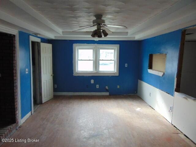 unfurnished bedroom with a tray ceiling, baseboards, and wood finished floors