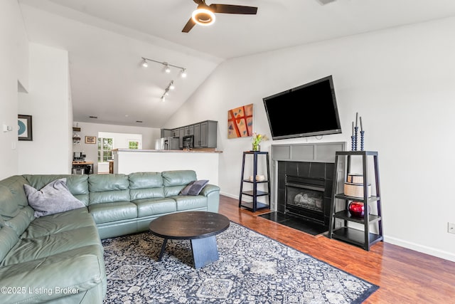 living area featuring vaulted ceiling, a ceiling fan, wood finished floors, baseboards, and a tile fireplace