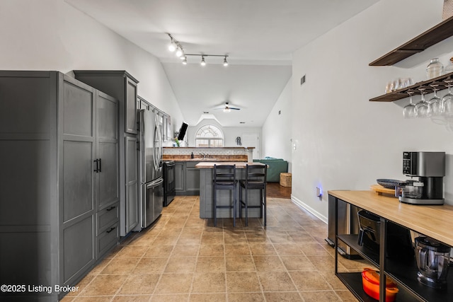 kitchen with freestanding refrigerator, a ceiling fan, a breakfast bar, lofted ceiling, and open shelves