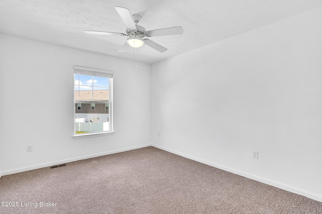 carpeted spare room with baseboards, a ceiling fan, a textured ceiling, and visible vents