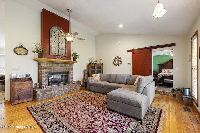 living room with ceiling fan, visible vents, vaulted ceiling, a barn door, and light wood finished floors