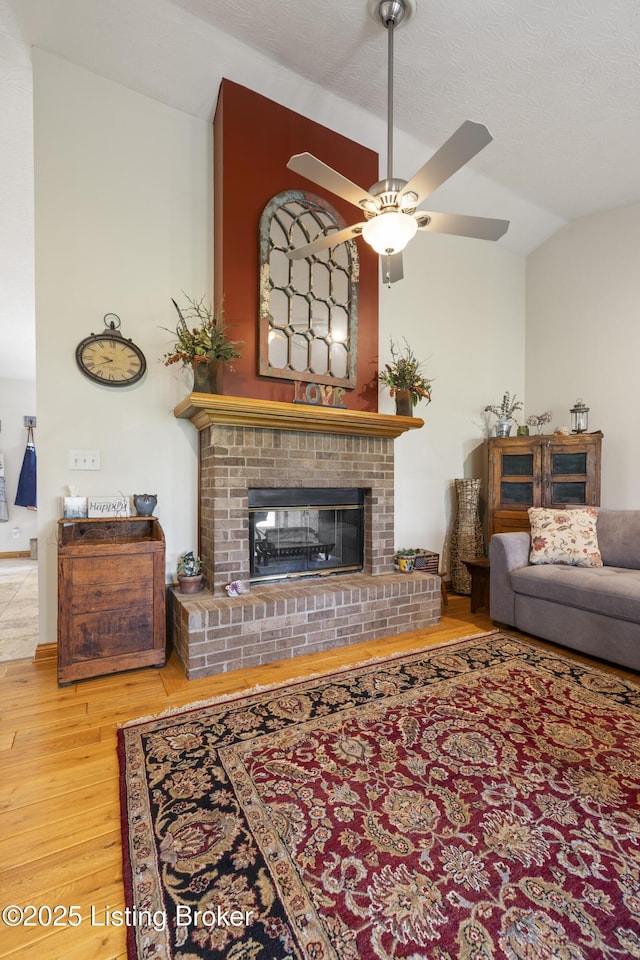 living room featuring vaulted ceiling, a fireplace, a ceiling fan, and wood finished floors