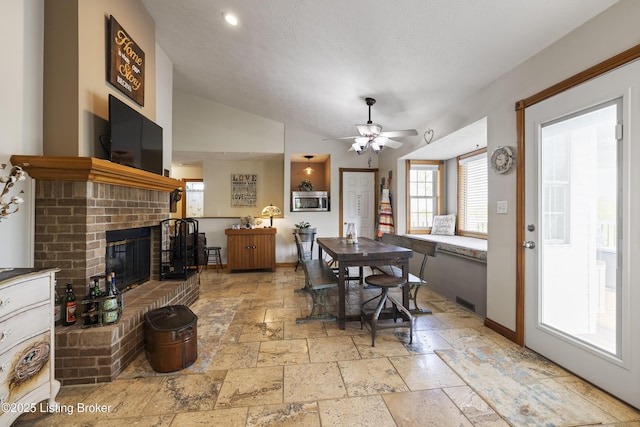 dining room with baseboards, stone tile floors, a ceiling fan, and a fireplace