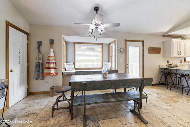 dining space with stone tile flooring, a ceiling fan, and baseboards