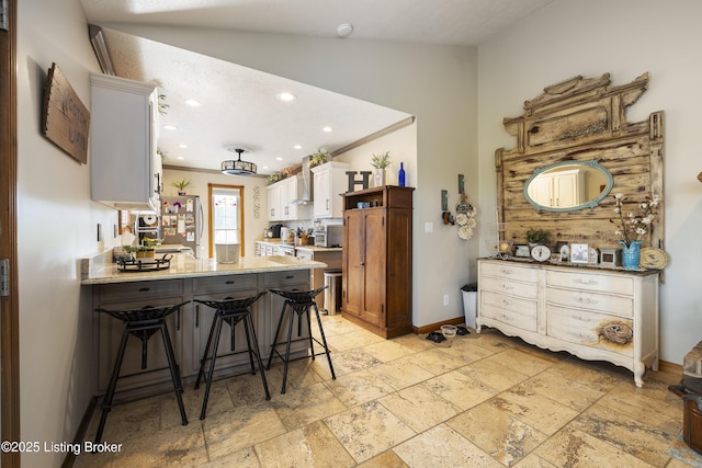kitchen featuring wall chimney range hood, vaulted ceiling, freestanding refrigerator, a peninsula, and stone tile flooring