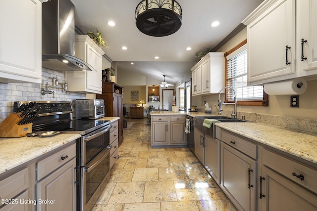 kitchen with stone tile floors, a ceiling fan, wall chimney exhaust hood, a sink, and double oven range