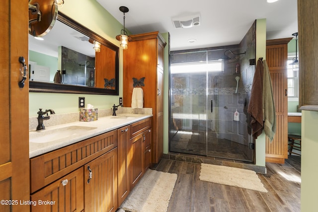 bathroom featuring visible vents, double vanity, wood finished floors, a sink, and a stall shower