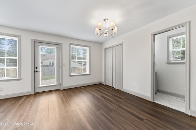 unfurnished dining area with baseboards, an inviting chandelier, wood finished floors, and visible vents