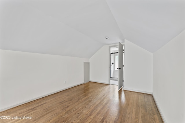 additional living space with baseboards, wood finished floors, and vaulted ceiling