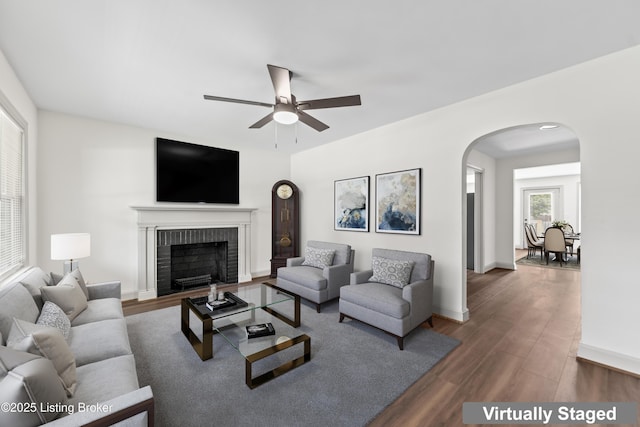 living room with wood finished floors, a fireplace, baseboards, ceiling fan, and arched walkways