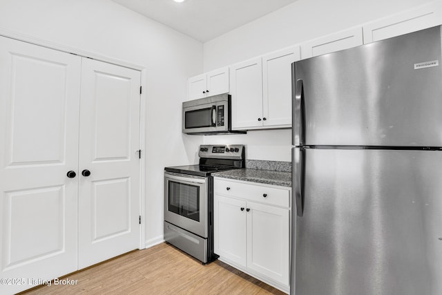 kitchen featuring white cabinets, appliances with stainless steel finishes, light wood-style flooring, dark stone counters, and baseboards