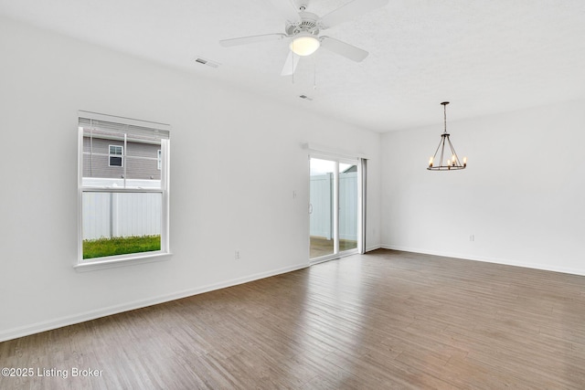 spare room featuring baseboards, visible vents, wood finished floors, and ceiling fan with notable chandelier