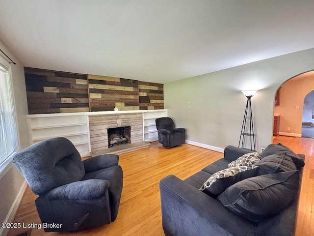 living area featuring arched walkways, wood finished floors, baseboards, a fireplace, and built in shelves