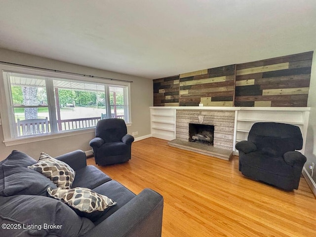 living room featuring wood finished floors, a stone fireplace, baseboards, and built in shelves