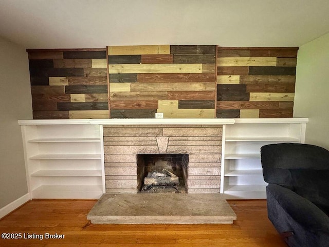 living area with wood finished floors, a fireplace, wooden walls, and baseboards