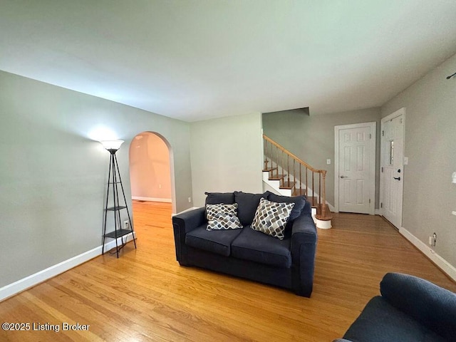 living room with arched walkways, stairway, wood finished floors, and baseboards