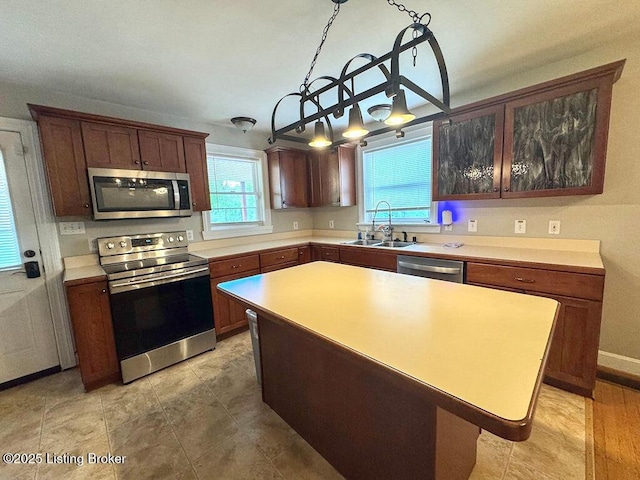 kitchen with appliances with stainless steel finishes, a sink, light countertops, a center island, and decorative light fixtures