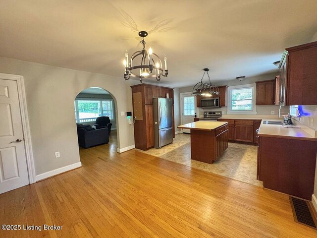 kitchen featuring appliances with stainless steel finishes, arched walkways, a kitchen island, light wood-type flooring, and a chandelier