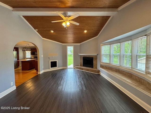 unfurnished living room with a tiled fireplace, wood ceiling, dark wood finished floors, ceiling fan, and arched walkways