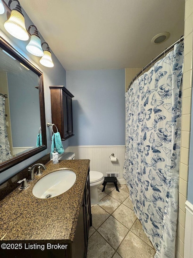 bathroom featuring a wainscoted wall, vanity, toilet, tile patterned floors, and curtained shower