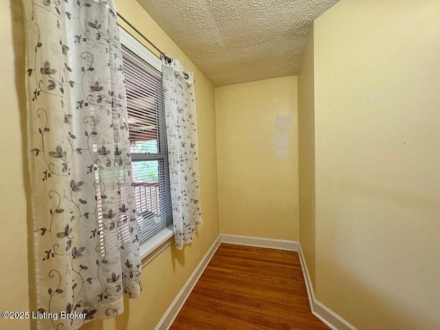 hallway featuring wood finished floors, a textured ceiling, and baseboards