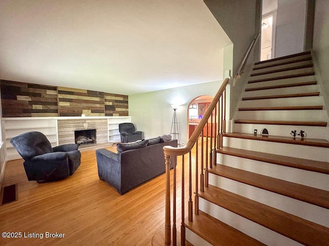 living area with stairway, light wood-style floors, a tile fireplace, and built in shelves