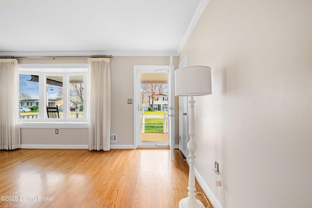 entryway featuring baseboards, ornamental molding, light wood finished floors, and visible vents